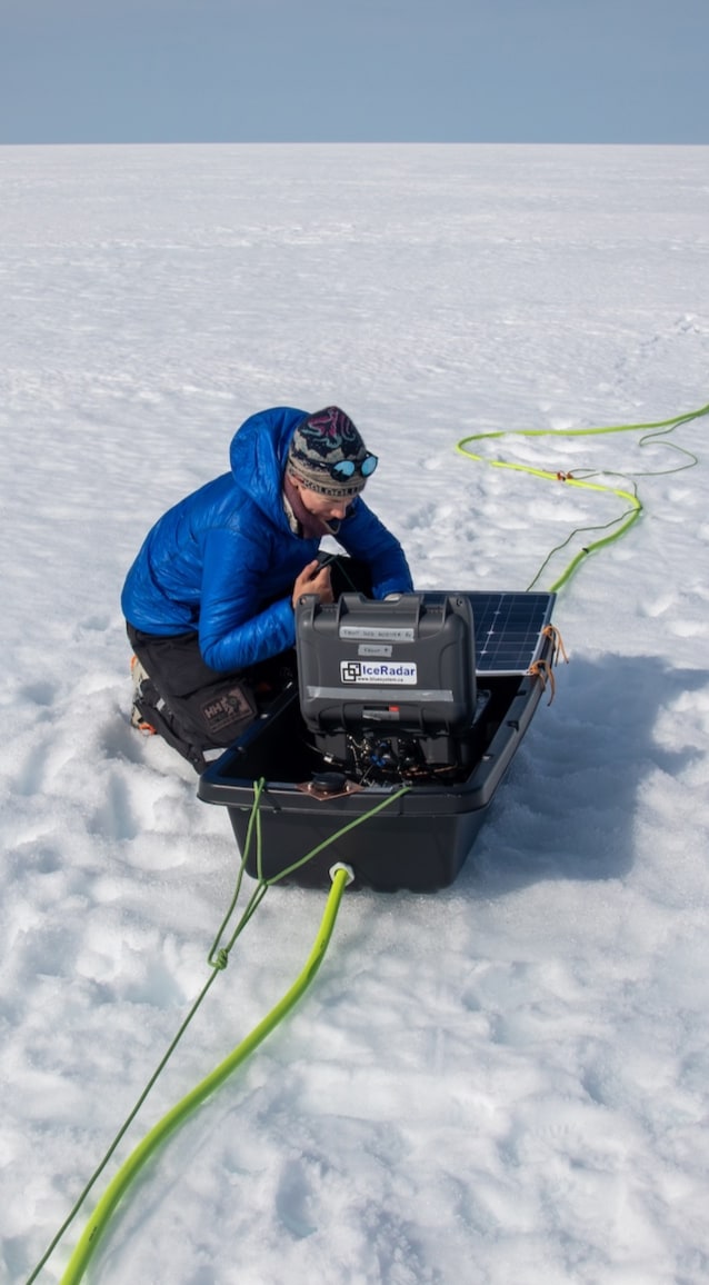 Heïdi est agenouillée près du radar, afférée aux ajustements du matériel, et entourée de la vaste étendue blanche de l'Antarctique.